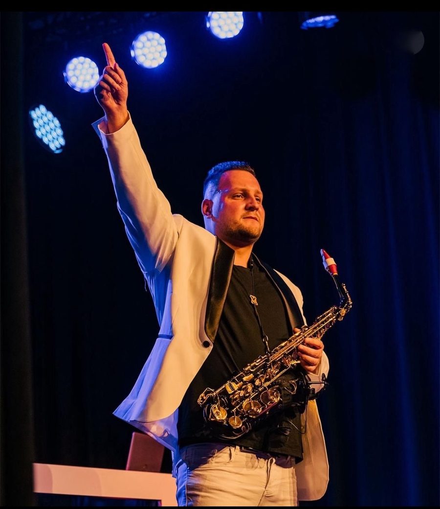 Enrico Braun im weißen Sakko mit Saxophon auf blau beleuchteter Bühne